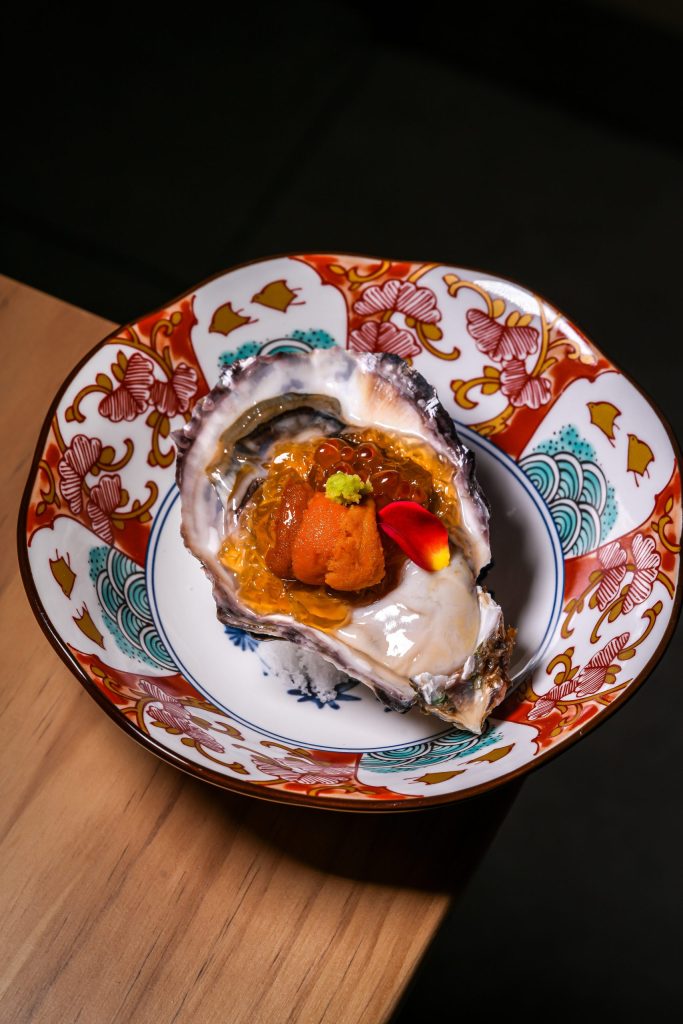 Oyster topped with uni, ikura and fresh wasabi, served on a red and gold Japanese plate